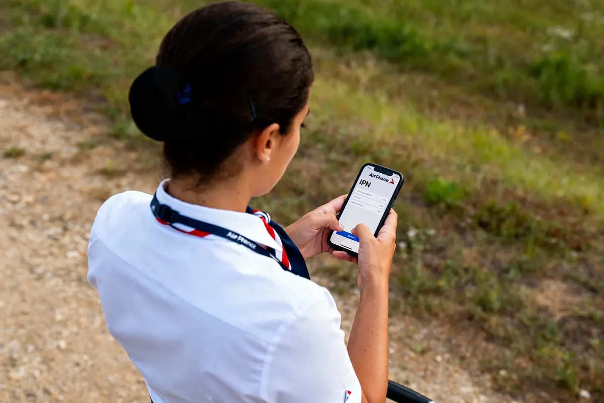Femme en uniforme Air France utilisant un smartphone, vérifiant des informations sur une application, arrière-plan herbeux.