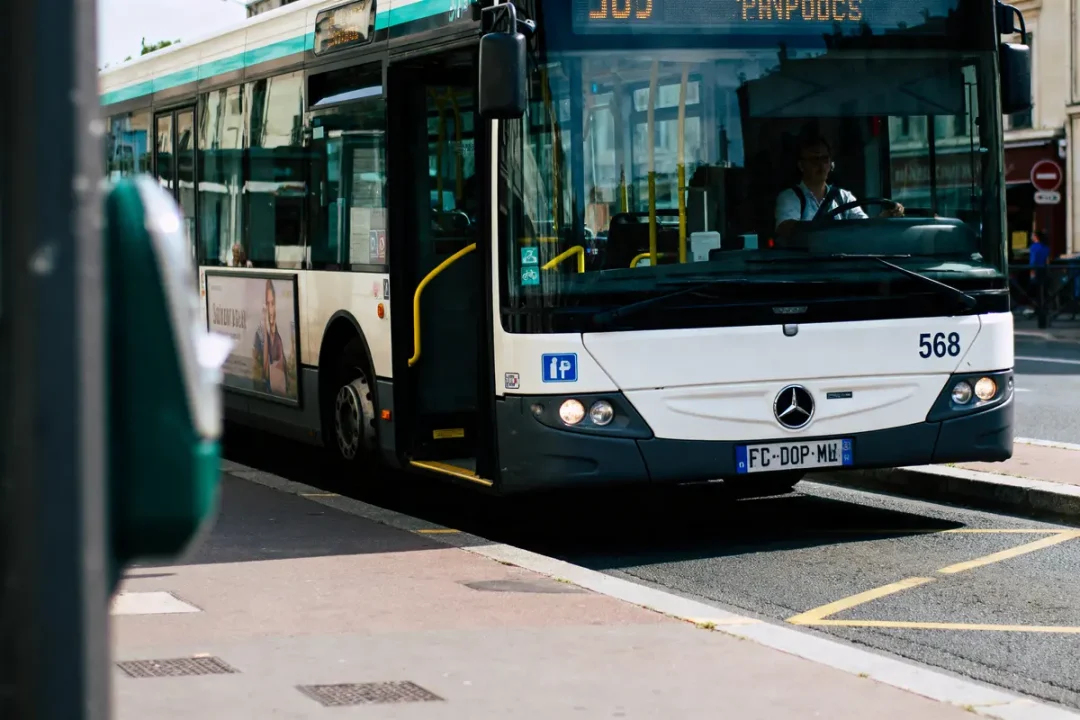 Autobus en service avec conducteur, vu de face, arrêt à un trottoir, panneau publicitaire visible.