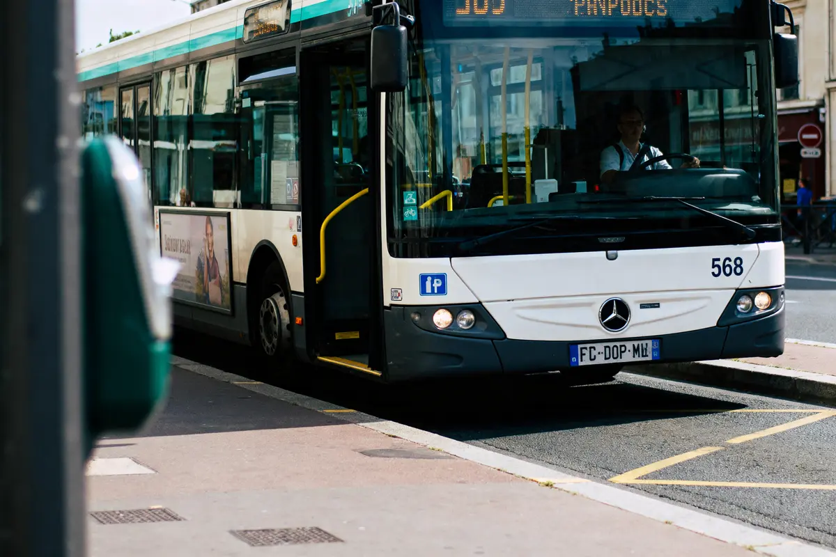 Autobus en service avec conducteur, vu de face, arrêt à un trottoir, panneau publicitaire visible.