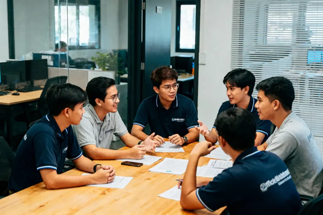 Six hommes en réunion, discutant autour d'une table avec des documents dans un bureau moderne.