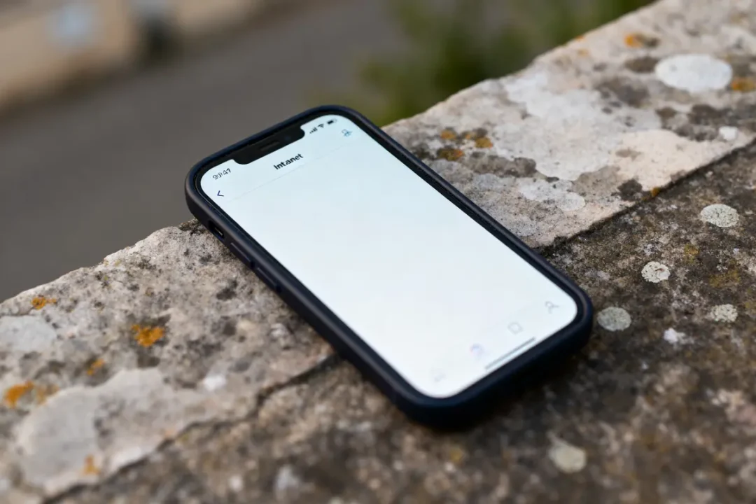 Smartphone noir sur muret en pierre, écran affichant "Intranet". Fond extérieur flou.