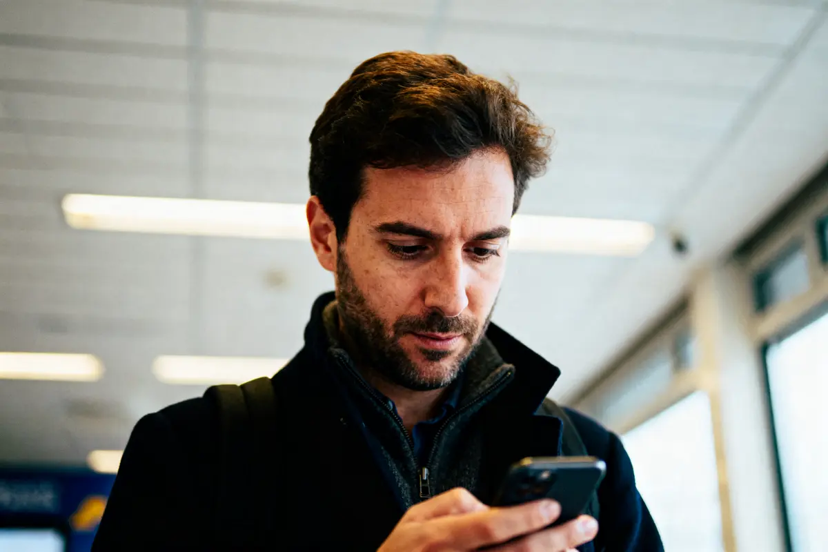 Un homme regarde son téléphone en intérieur, lumières en arrière-plan floues.