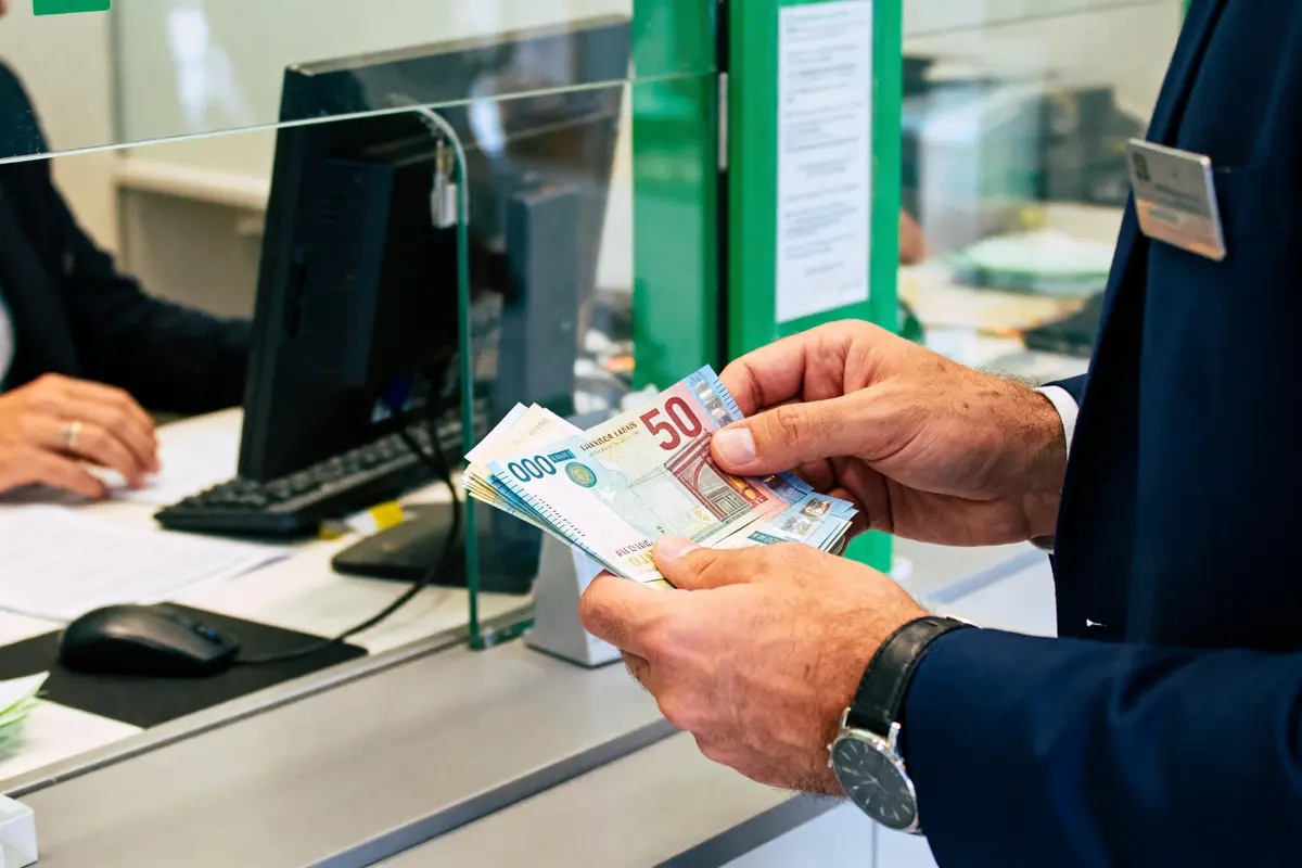 Un homme manipule des billets derrière une vitre, dans un bureau de change ou banque.