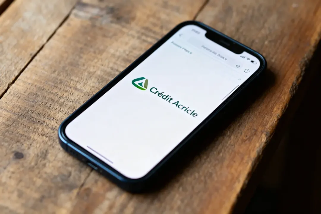 Smartphone affichant le logo "Crédit Agricole" sur un écran, posé sur une table en bois rustique.
