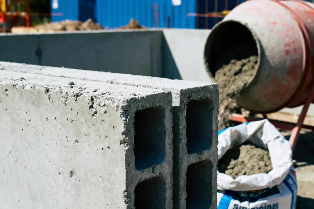 Parpaings devant bétonnière et sac de ciment sur chantier de construction.