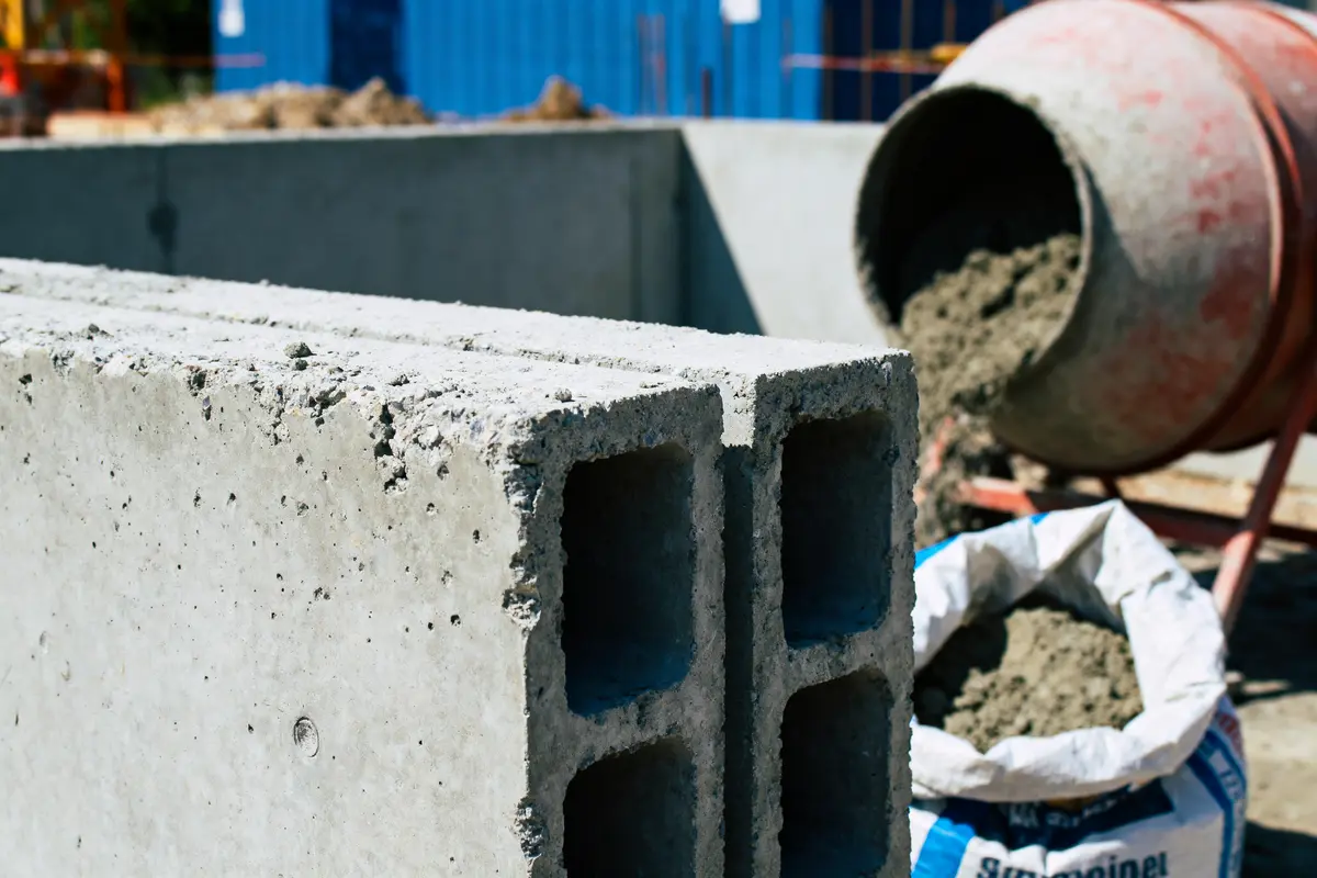 Parpaings devant bétonnière et sac de ciment sur chantier de construction.