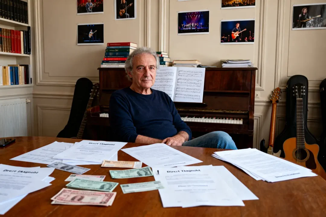 Homme assis devant un piano entouré de papiers, billets, guitares, photos de concerts.