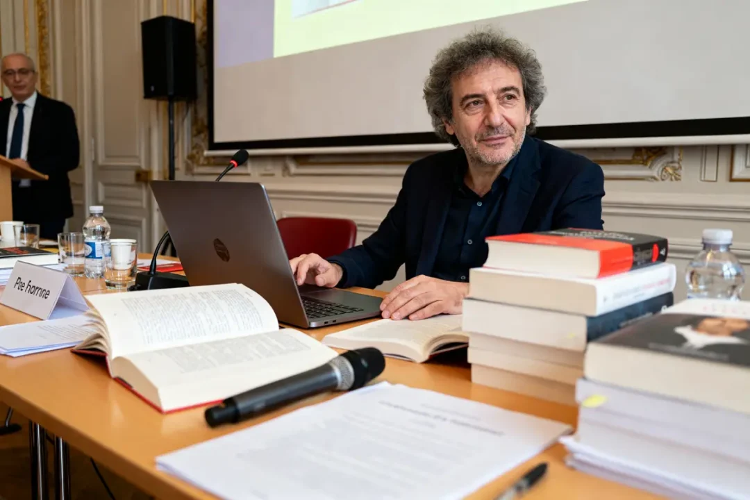 Homme avec ordinateur et livres évoquant la fortune de Michel Onfray en conférence.