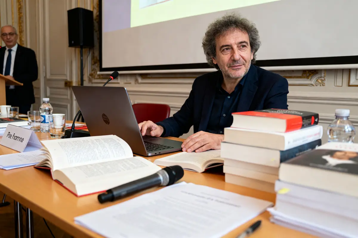 Homme avec ordinateur et livres évoquant la fortune de Michel Onfray en conférence.