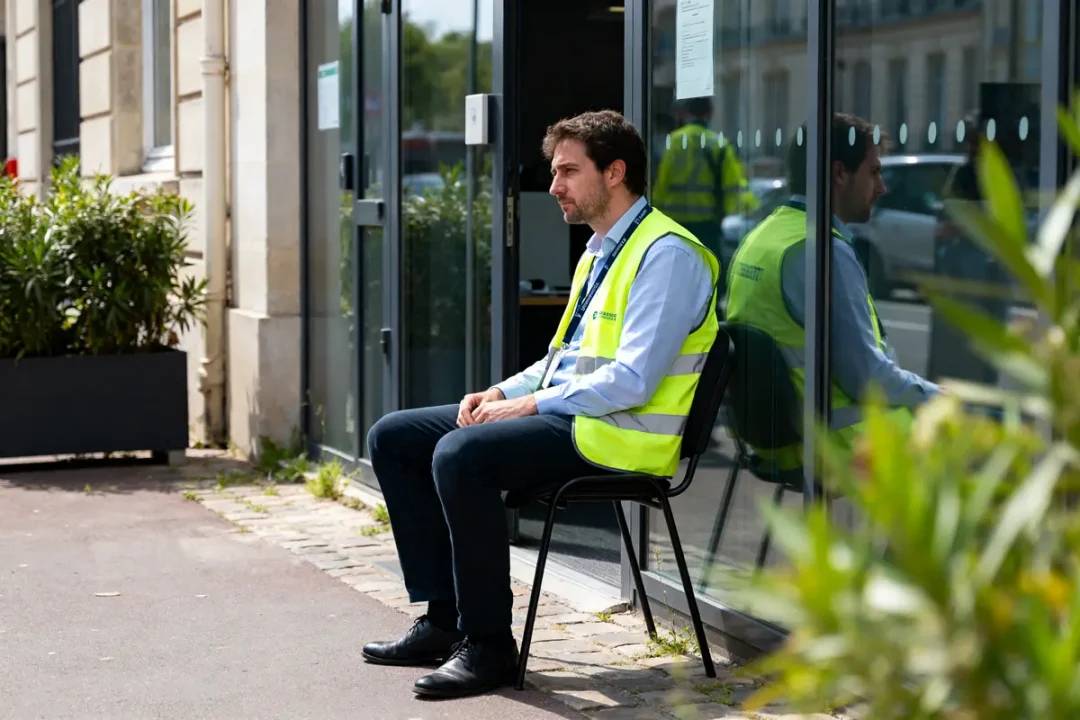 Un homme en gilet réfléchissant assis devant un bâtiment, rtt en intérim.