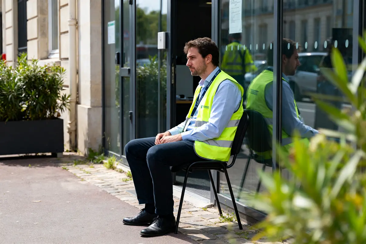 Un homme en gilet réfléchissant assis devant un bâtiment, rtt en intérim.